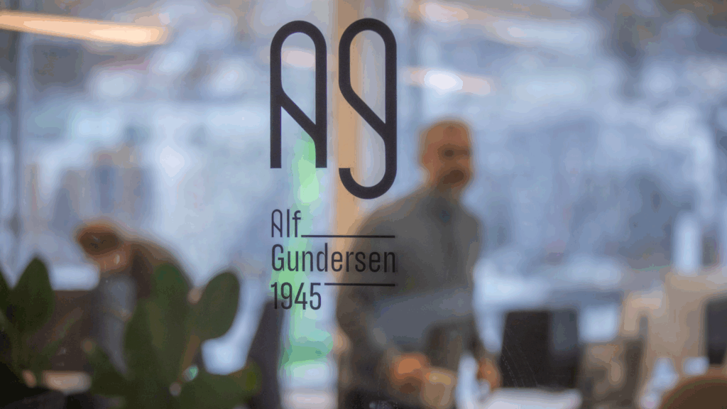 Bilde av ansatt på kontoret til Alf Gundersen bak inngangsdør med byråets logo